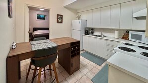 A compact kitchen with white cabinets, a stove, and a sink. There's a small dining area with a table and chairs. - Cozy One Bedroom Basement Apt with Free Parking (Markham)