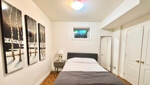 A bedroom with a bed, a nightstand, a window, and a door. - Cozy One Bedroom Basement Apt with Free Parking (Markham)