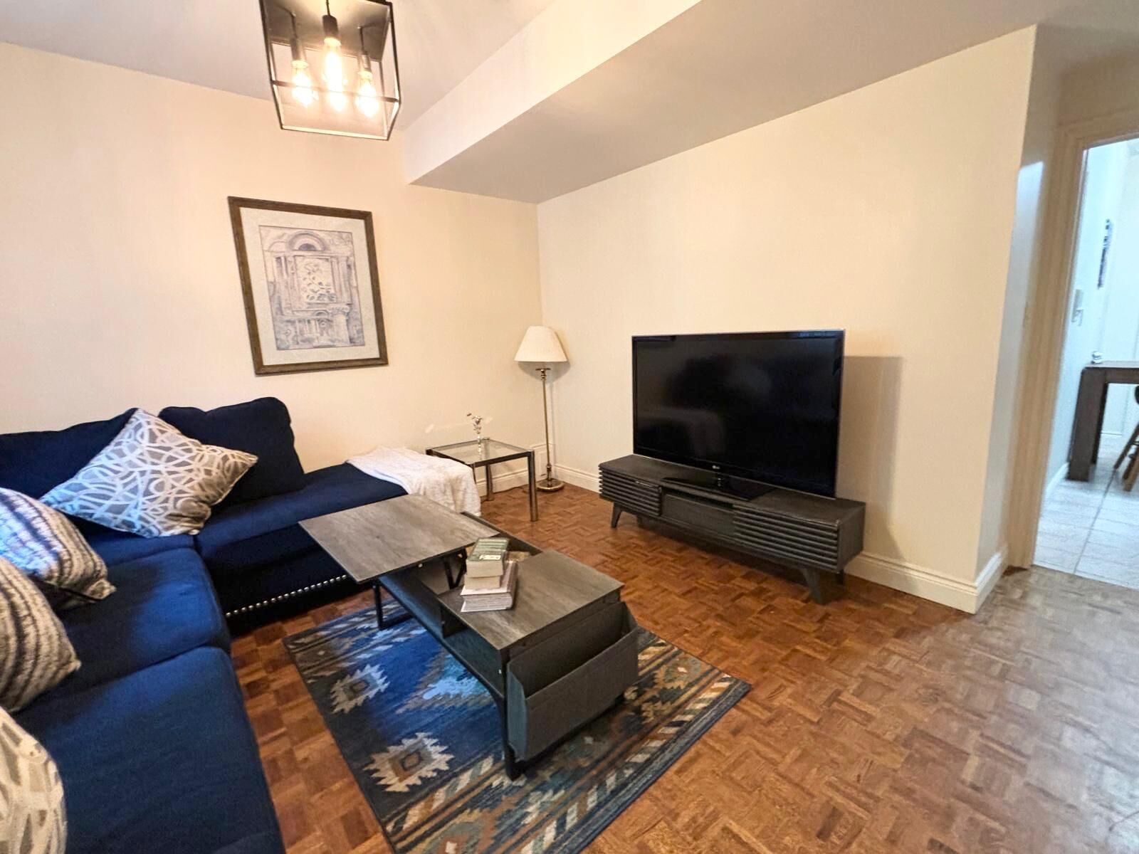 Uma sala de estar com sofá azul, mesa de centro, rack para TV e tapete estampado.