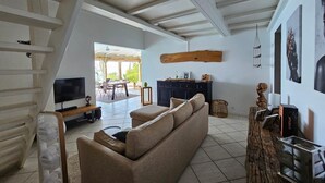 A spacious living room with a sofa, a TV, a wooden cabinet, and a large wooden beam on the ceiling. - Villa Kaz in Thomy, pool and Spa Panoramic sea view of Pointe Noire bay (Pointe-Noire)