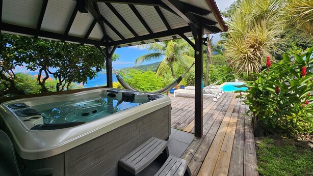 A hot tub under a wooden pergola with a view of a pool and lush greenery. - Villa Kaz in Thomy, pool and Spa Panoramic sea view of Pointe Noire bay (Pointe-Noire)