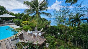 A wooden deck with a pool, white lounge chairs, and a palm tree. - Villa Kaz in Thomy, pool and Spa Panoramic sea view of Pointe Noire bay (Pointe-Noire)