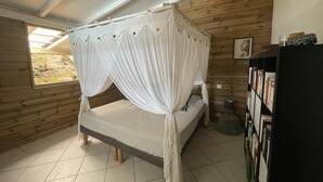 A room with a bed under a canopy, wooden walls, a bookshelf, and a window with a view. - Villa Kaz in Thomy, pool and Spa Panoramic sea view of Pointe Noire bay (Pointe-Noire)