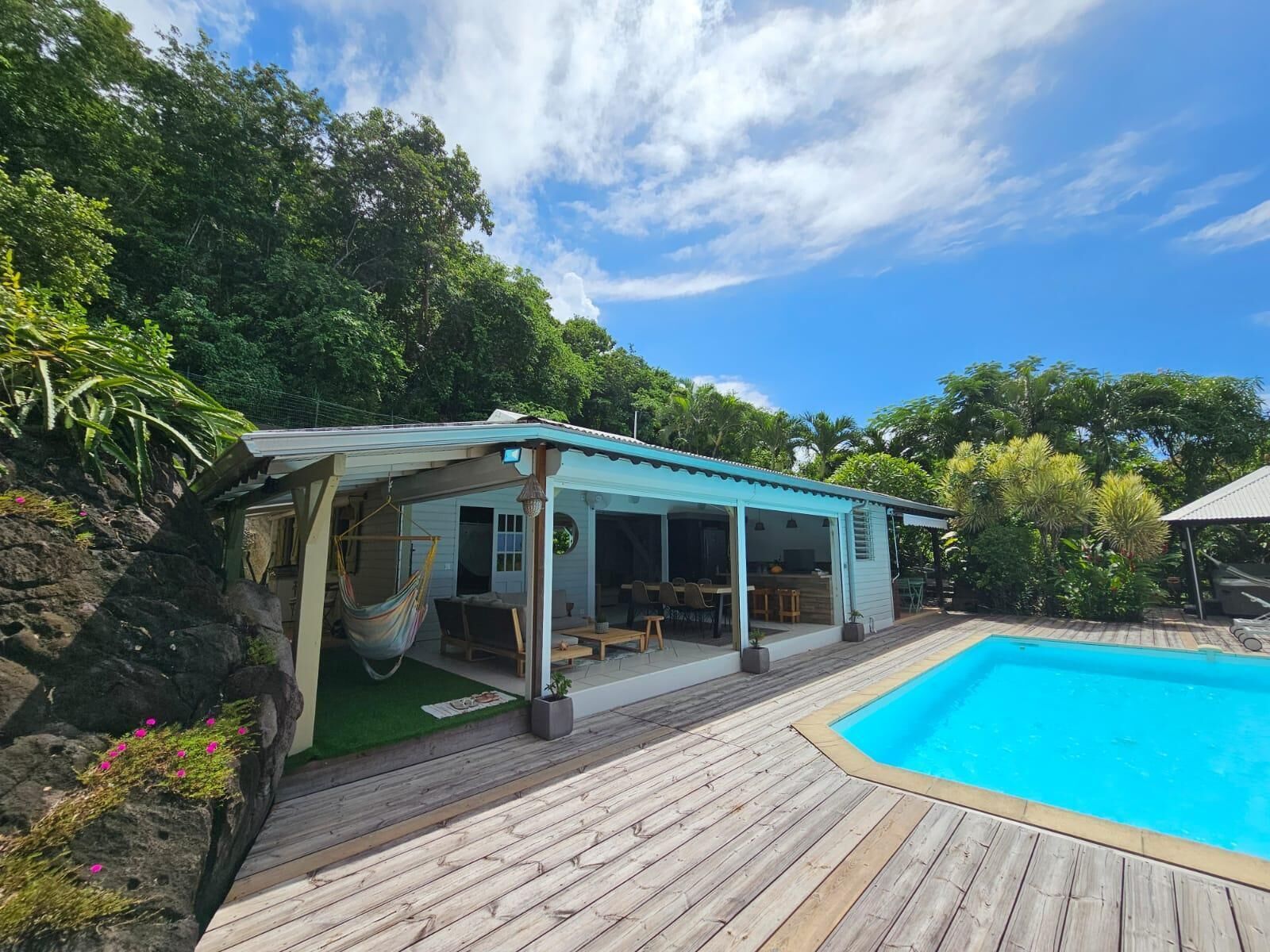 A house with a pool, surrounded by lush greenery and a wooden deck.