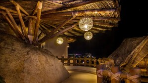 Ein Gebäude mit einem Reetdach, das mit hängenden, kugelförmigen Lampen, einer Steinmauer und einem Holzzaun versehen ist.