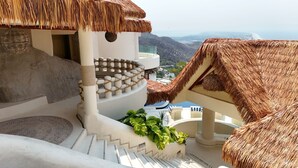 Eine Treppe unter einem Reetdach, die zu einem Balkon mit Blick auf die Landschaft führt.