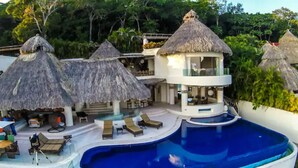 Ein Resort mit Swimmingpool, strohgedeckten Gebäuden und Liegebereichen.