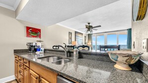 A kitchen with granite countertops, stainless steel appliances, wooden cabinets, and a view to the outside. - Dunes of Panama 1104e (Panama City Beach)