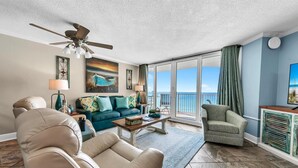 A spacious living room with a large window offering a view of the ocean, a ceiling fan, and a cozy seating area with a sofa and chairs. - Dunes of Panama 1104e (Panama City Beach)