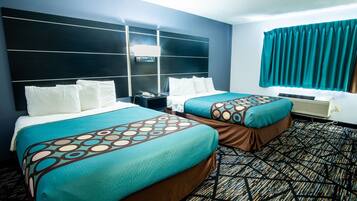 A hotel room with two beds, a large headboard, a window with curtains, and a patterned carpet.