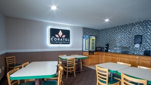 A Coratel Inn & Suites restaurant with wooden tables and chairs, a tiled backsplash, and a sign above the counter.