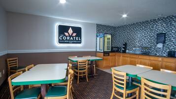 A Coratel Inn & Suites restaurant with wooden tables and chairs, a tiled backsplash, and a sign above the counter.
