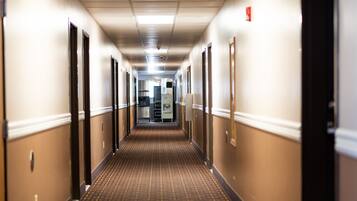 A hotel hallway with a patterned carpet, beige walls, and doors on both sides.