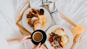 Un plateau de petit-déjeuner avec des œufs, des saucisses, des toasts et une tasse de café, posé sur un lit.
