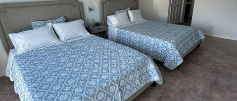 Een hotelkamer met twee bedden, een plafondventilator en een deur naar een andere kamer.