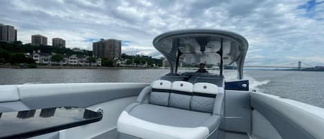 A boat with a covered seating area, a table, and a view of a cityscape and bridge in the background.