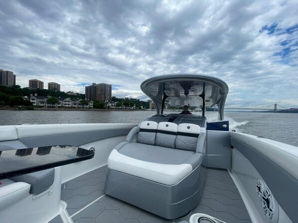 A boat with a covered seating area, a table, and a view of a cityscape and bridge in the background.