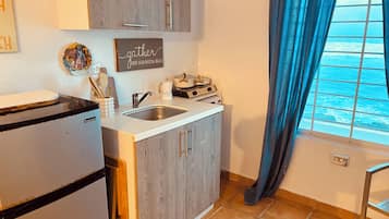 Una cocina con un fregadero, estufa y armarios. Hay una ventana con cortinas y vista al océano.