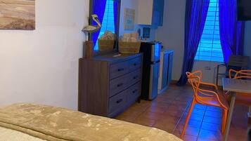 Una habitación de hotel con cama, escritorio con silla, cómoda, ventana con cortinas y un adorno de pez montado en la pared.