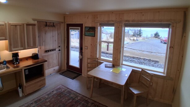 Eine kompakte Küche mit Holzausstattung, einem Esstisch mit Stühlen, einer Kaffeemaschine und Blick auf einen Parkplatz durch große Fenster.