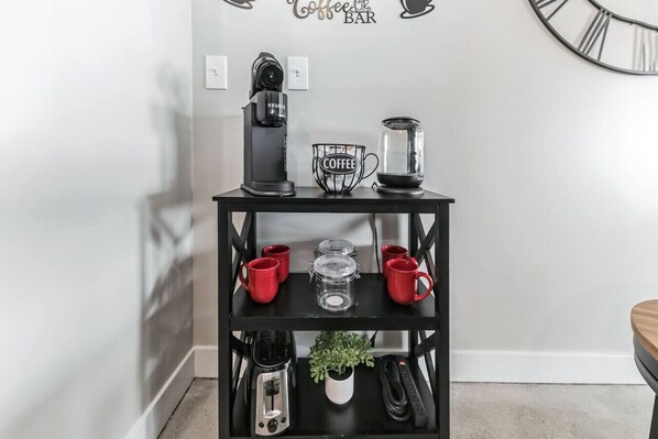 Una estación para café con café negro, una cafetera Keurig, una jarra de café y una taza sobre un estante negro.
