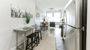 A modern kitchen with a stainless steel refrigerator, a dining area with a table and chairs, and a large window providing natural light. - Walk to Bengals, Reds, Free Parking, King Bed, Gym (Cincinnati)