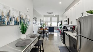 A modern kitchen with stainless steel appliances, a dining area with a round table and chairs, and a living space with a large window. - Walk to Bengals, Reds, Free Parking, King Bed, Gym (Cincinnati)