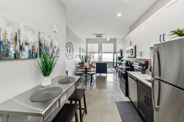 A modern kitchen with stainless steel appliances, a dining area with a round table and chairs, and a living space with a large window. - Walk to Bengals, Reds, Free Parking, King Bed, Gym (Cincinnati)