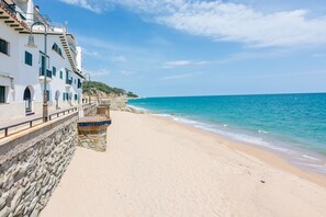 Ein Küstengebäude mit einer Steinmauer, einem Balkon und Blick auf Strand und Meer.
