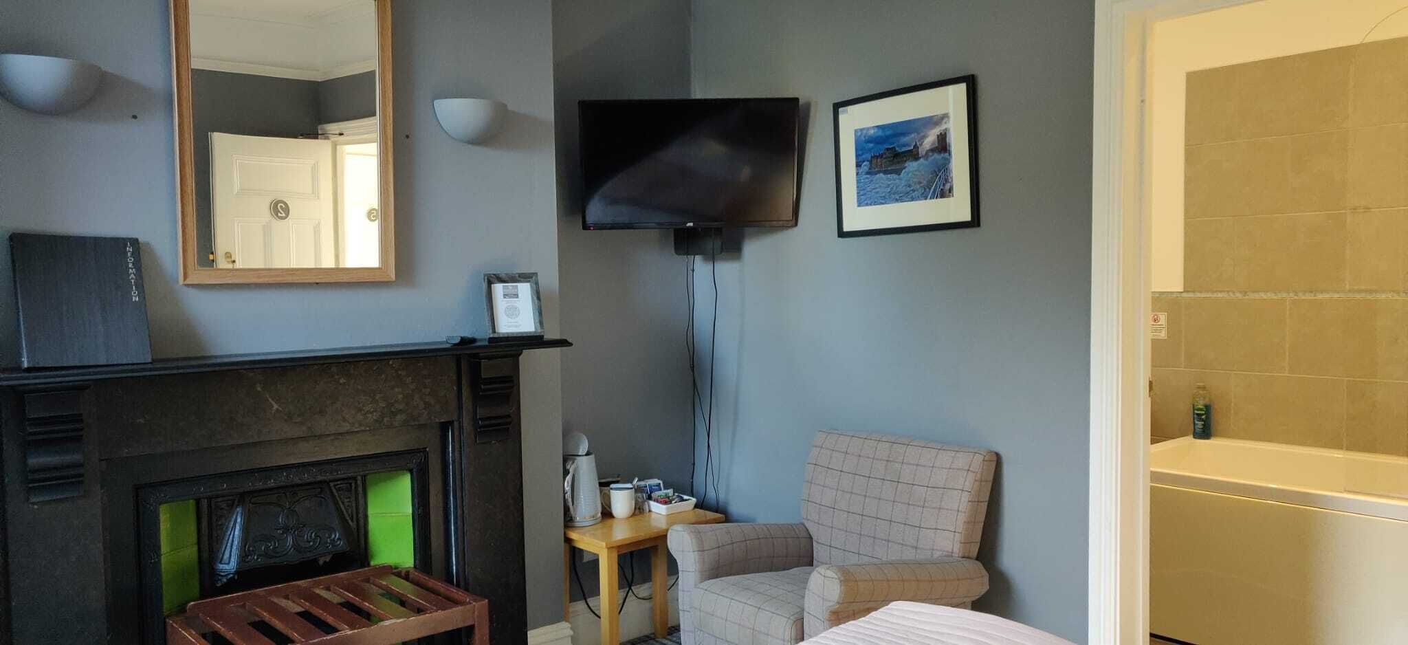 Ein Hotelzimmer mit Kamin, einem an der Wand befestigten Fernseher, einem gerahmten Bild und einer Badewanne.