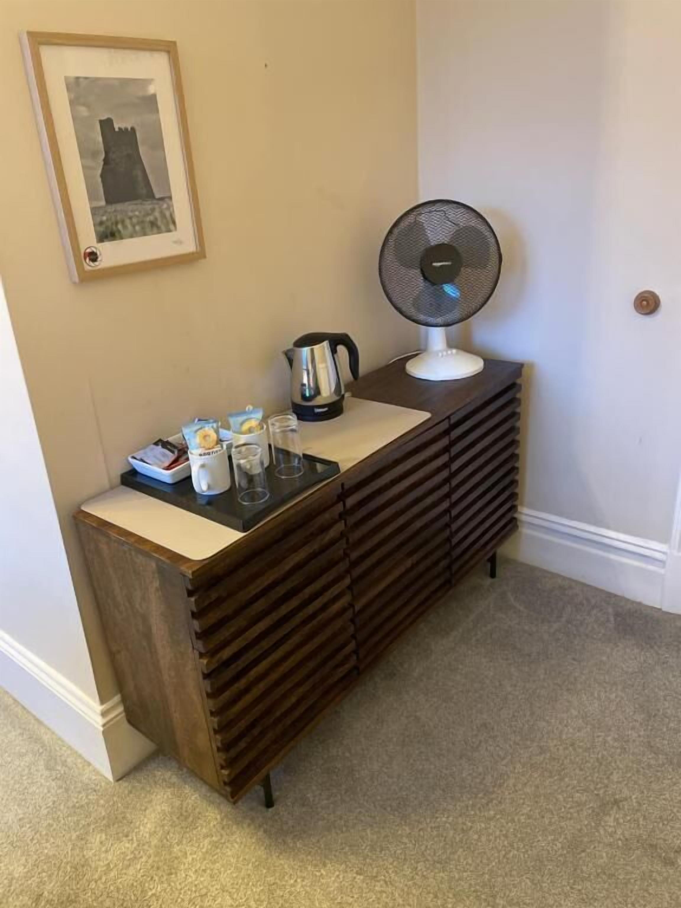 A wooden dresser with a kettle, a fan, and a framed picture on the wall.