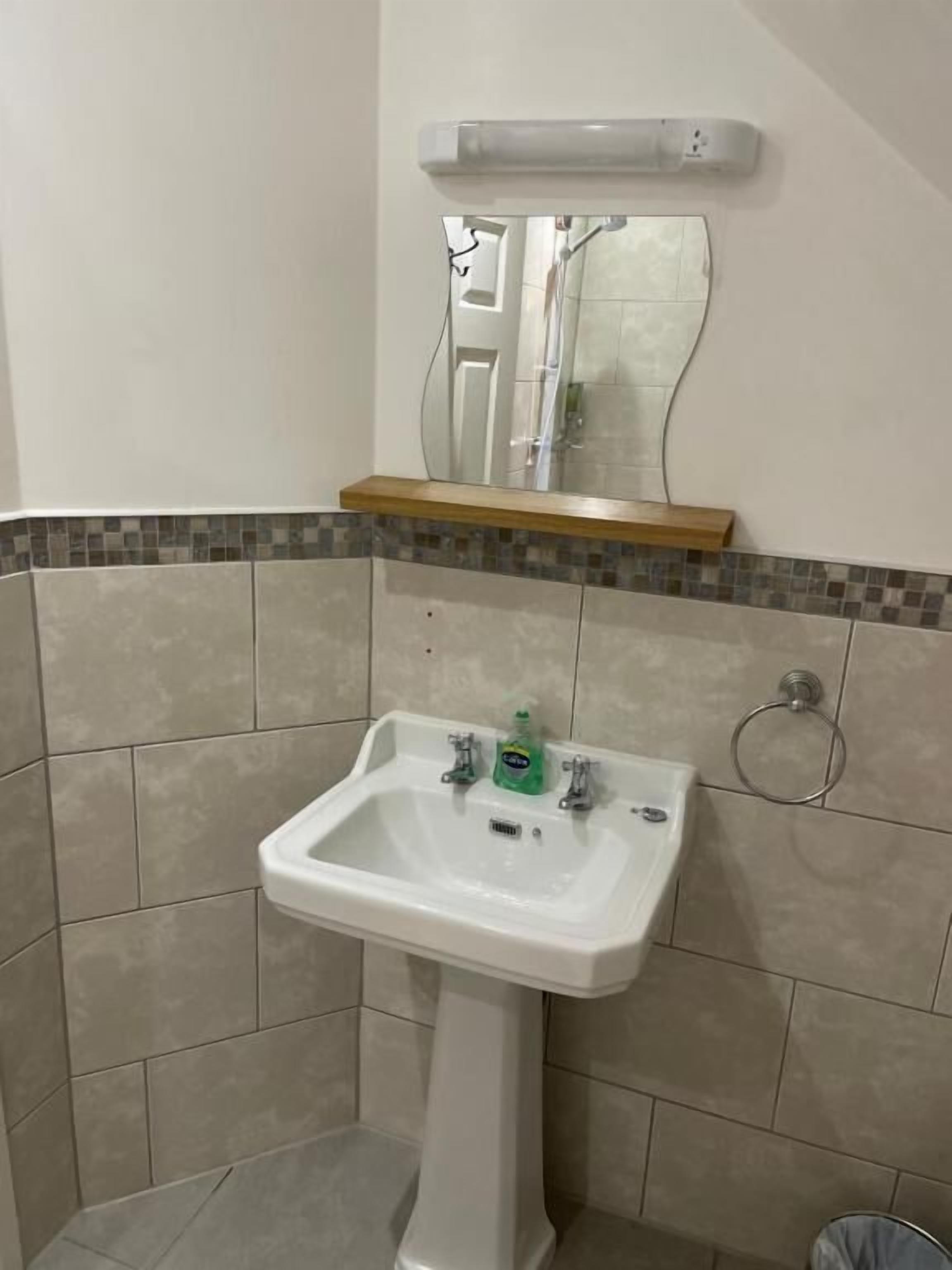 A bathroom with a white sink, a mirror, and a soap dispenser.