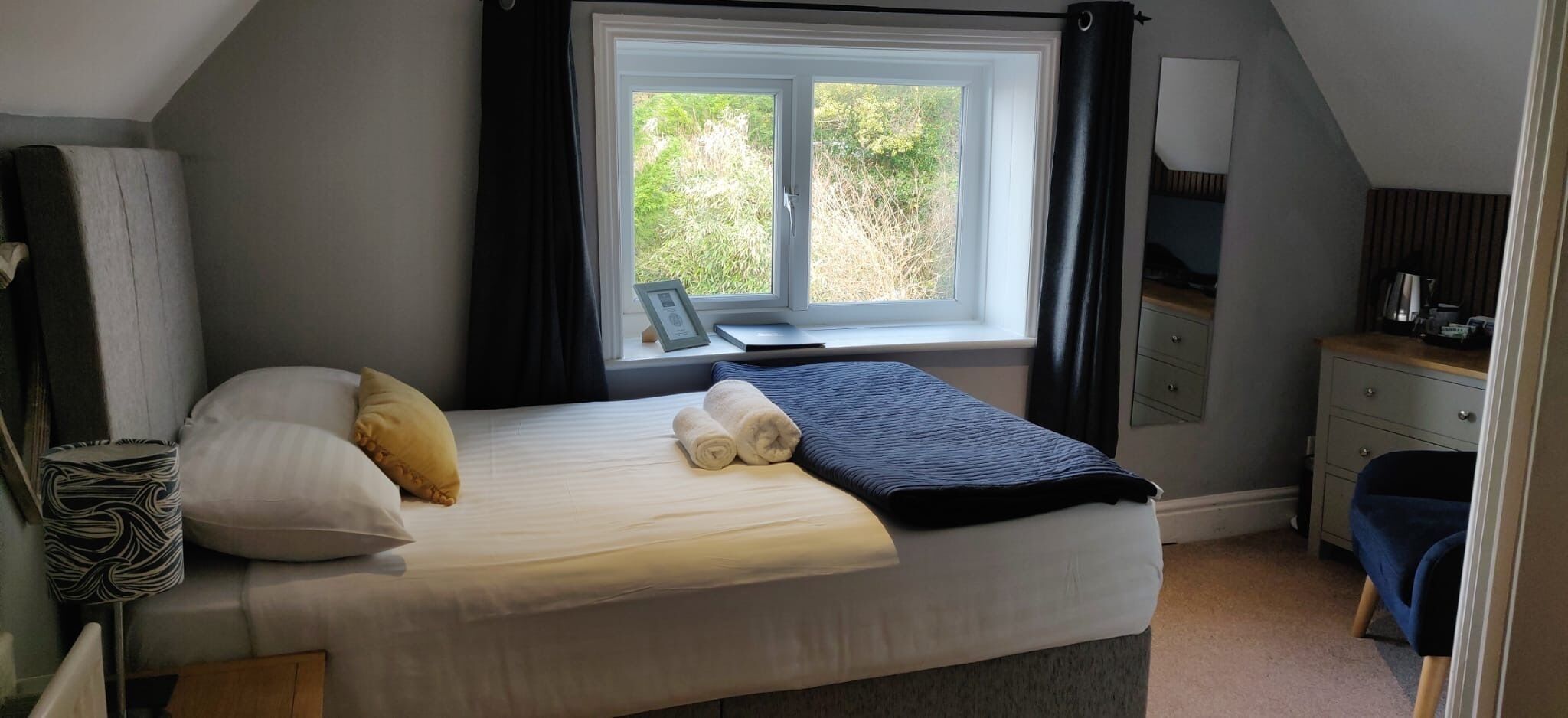 A bedroom with a bed, a desk, and a window with curtains.
