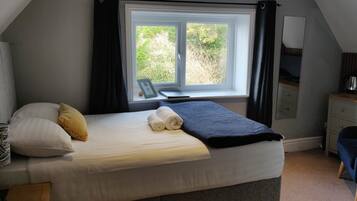 A bedroom with a bed, a desk, and a window with curtains.