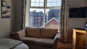 A cozy room with a sofa, a bed, a TV, and a window with curtains. - Bodalwyn Guest House (Aberystwyth)
