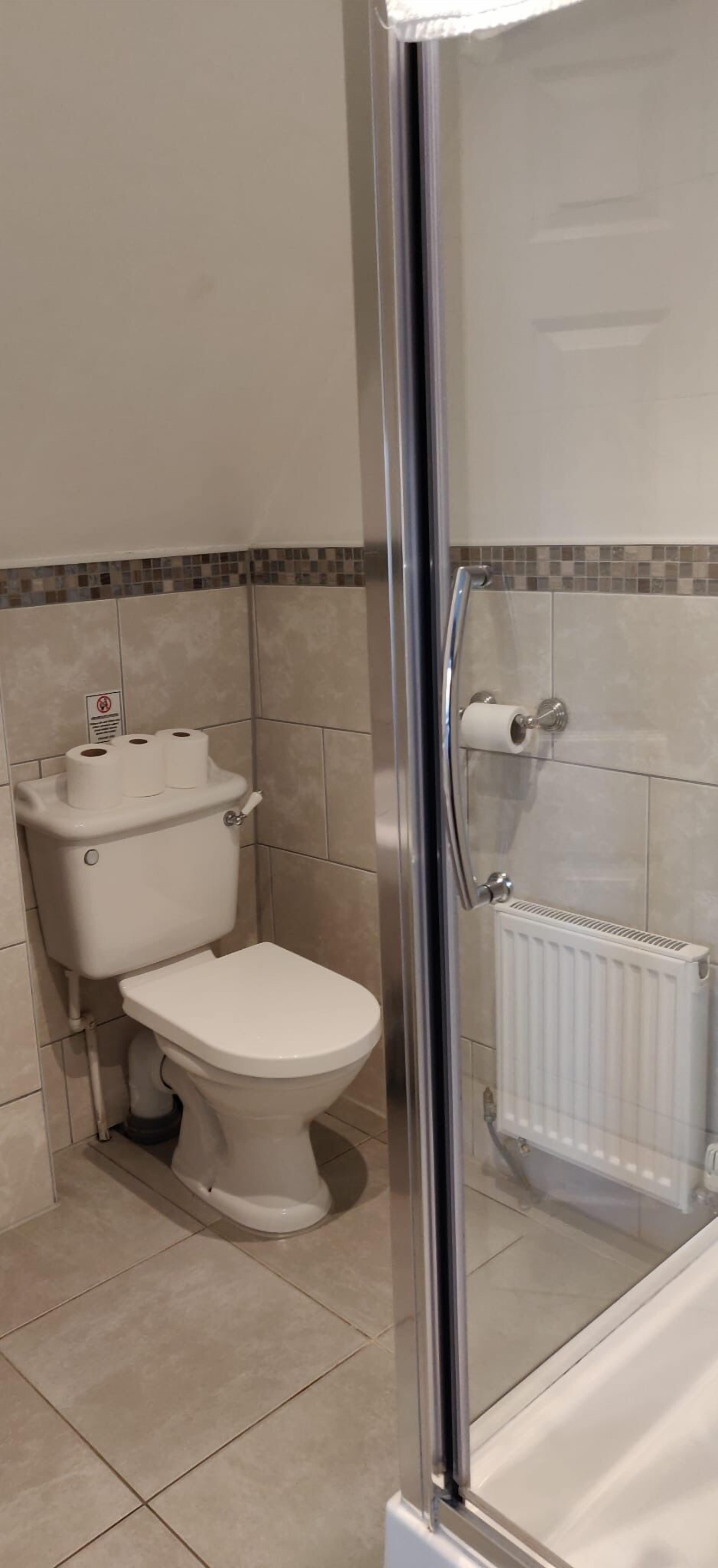Un baño con inodoro, cabina de ducha de vidrio y suelo de baldosas.
