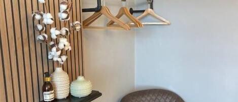 Une pièce d’angle avec un fauteuil en cuir marron, un mur lambrissé en bois, un portant à vêtements noir en bois et des vases décoratifs.