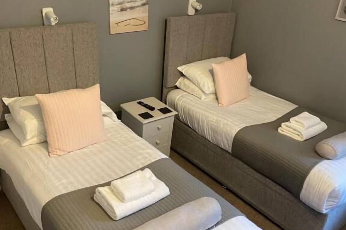 A hotel room with two beds, each with a headboard, a nightstand, and a small table.