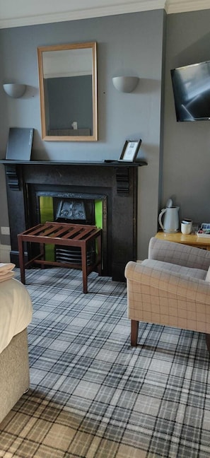 A living room with a fireplace, a sofa, a coffee table, and a television mounted on the wall. - Bodalwyn Guest House (Aberystwyth)