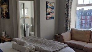 A hotel room with a bed, a sofa, a bathroom with a sink, and a window with a view of buildings. - Bodalwyn Guest House (Aberystwyth)