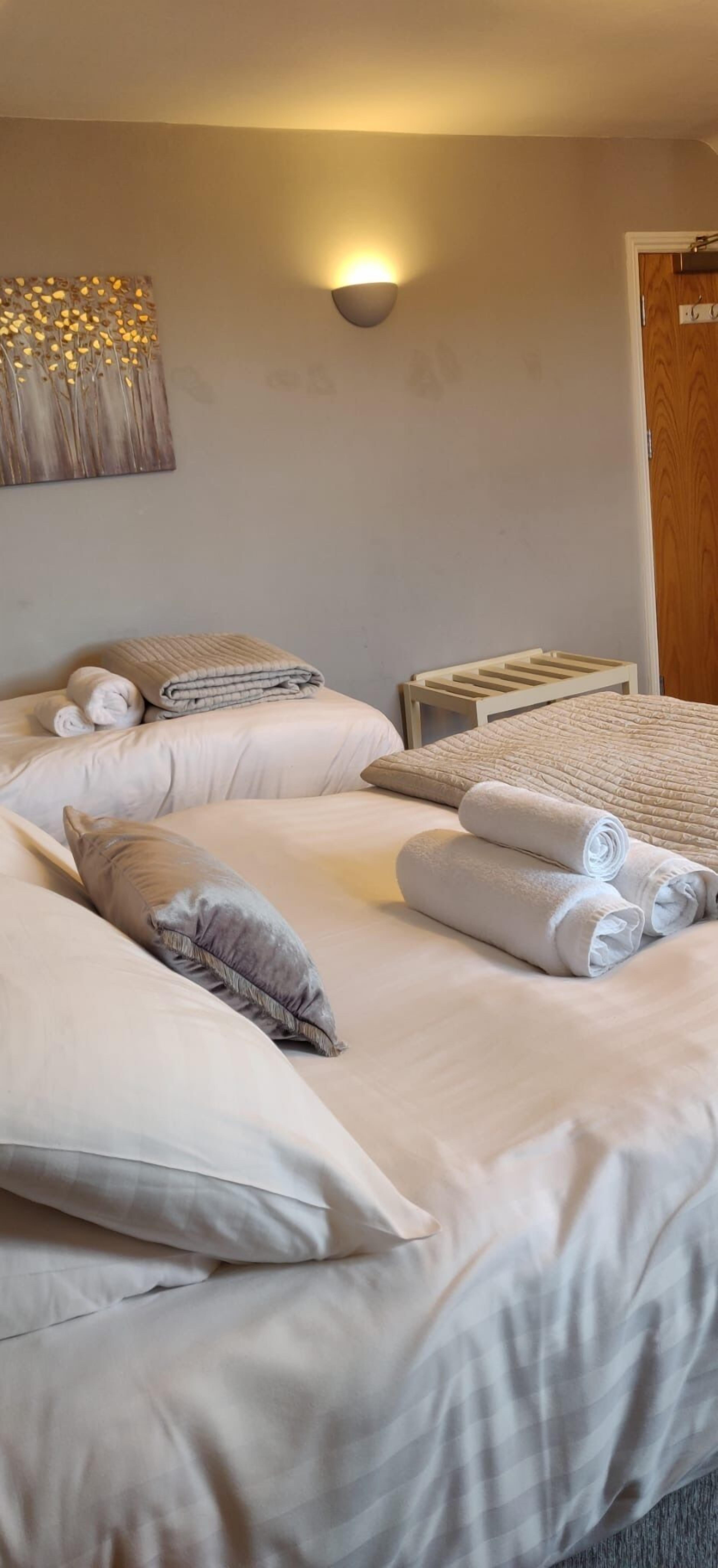 Un lit bien fait, avec du linge de lit blanc et des serviettes pliées, un luminaire fixé au mur et une porte en bois.