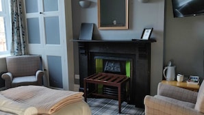 A room with a fireplace, a bed, two armchairs, a small table, and a television on the wall. - Bodalwyn Guest House (Aberystwyth)