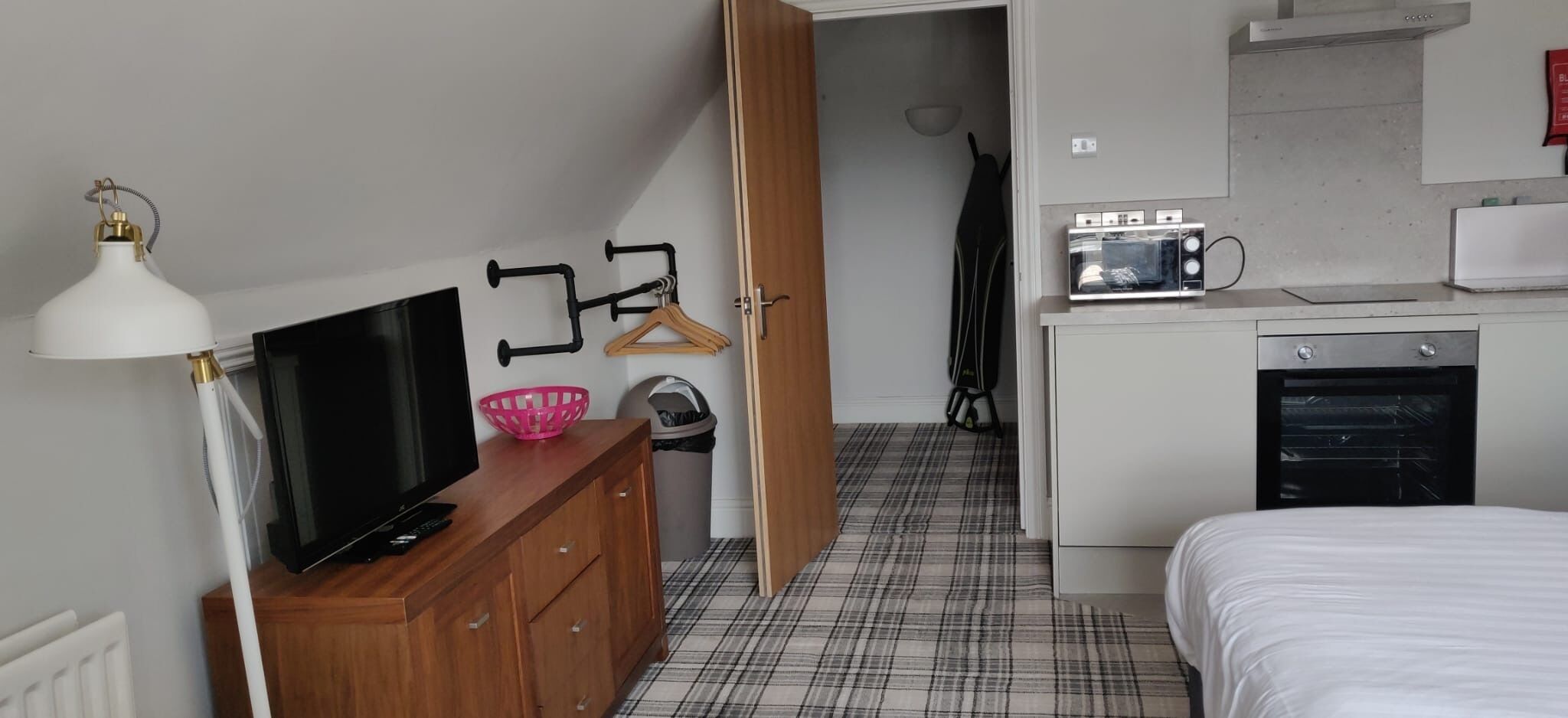 Un dormitorio con televisión, cómoda y kitchenette que incluye microondas y tostadora.