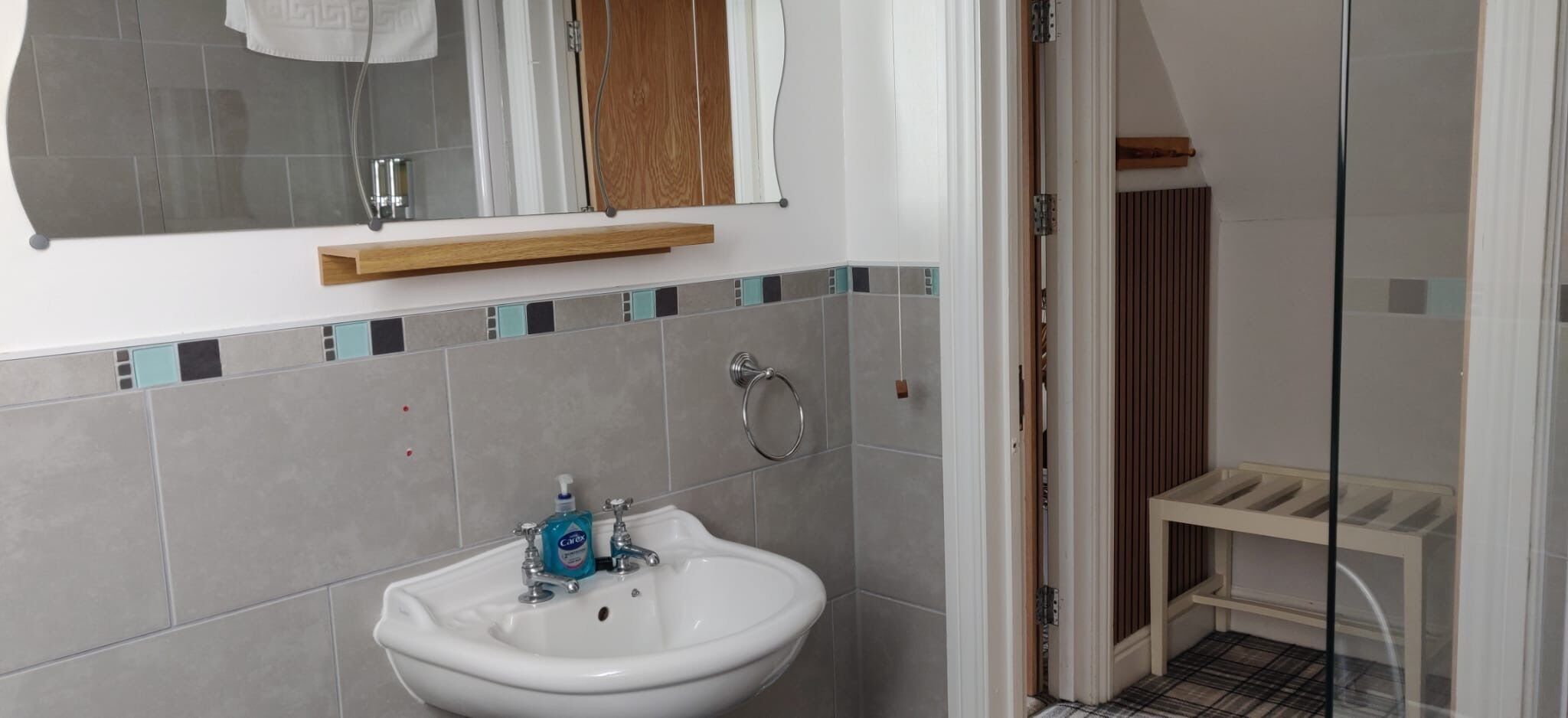 Een badkamer met een witte wastafel, een spiegel en een houten plank erboven.