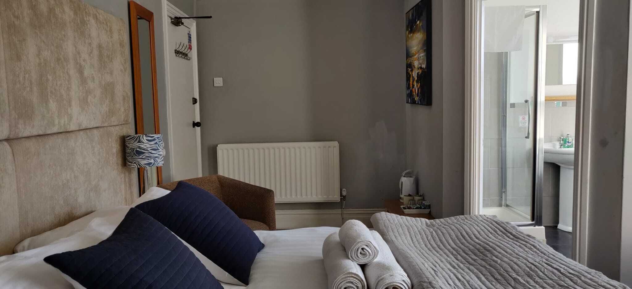 Habitación de hotel con cama, radiador, toallero y vista al baño.