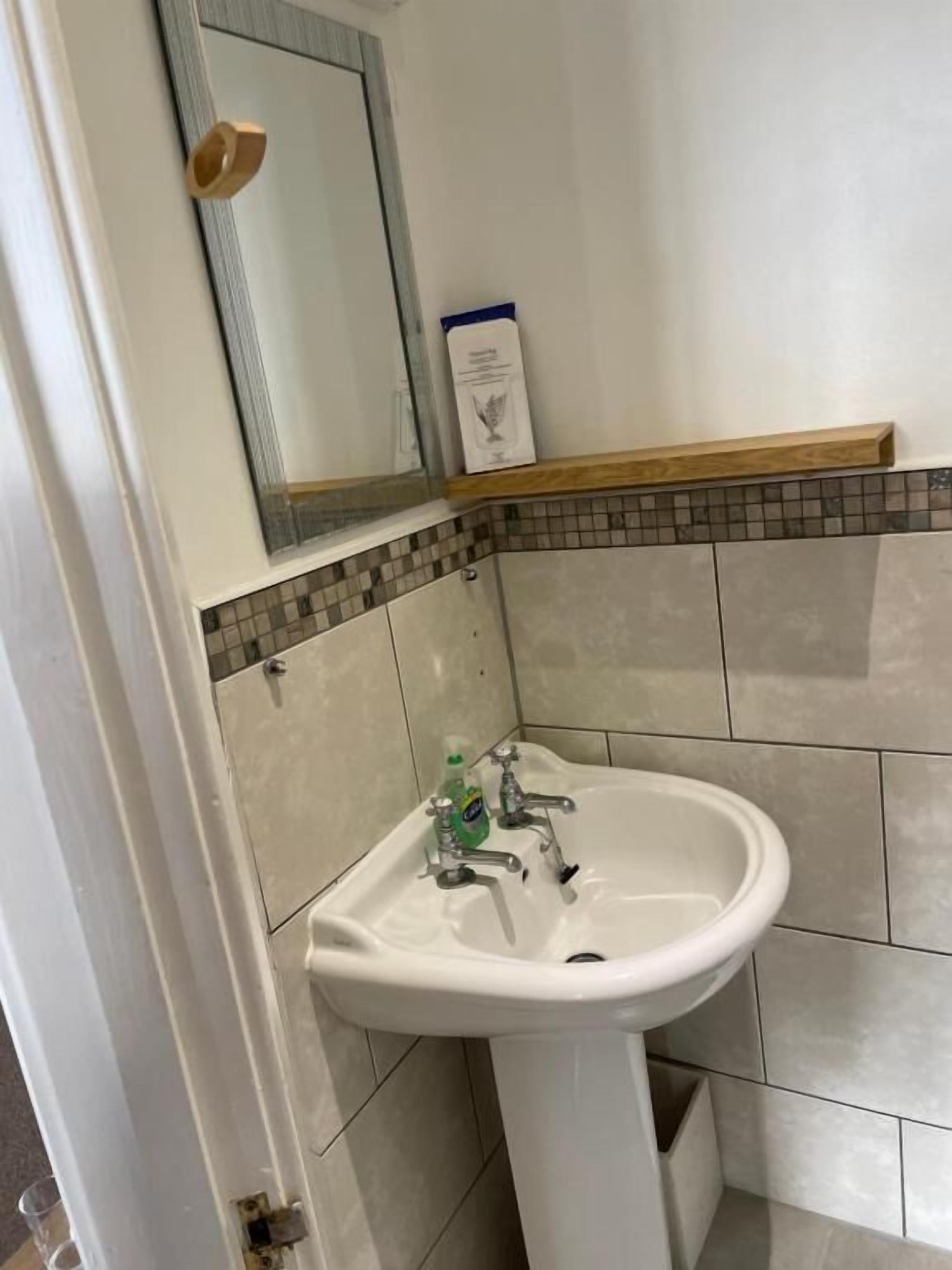Un baño con un lavabo blanco, un espejo y una repisa con una caja.
