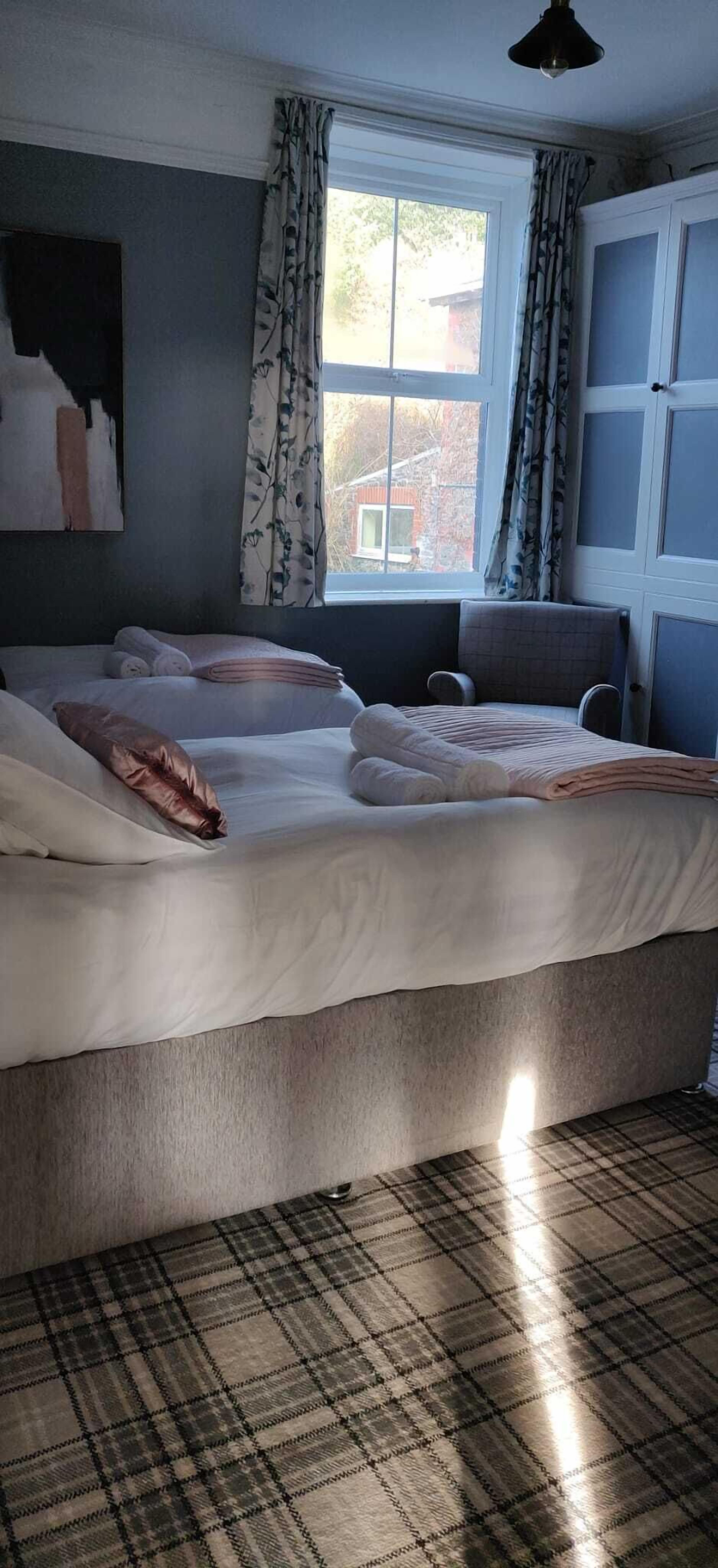 A bedroom with a bed, a chair, a window with curtains, and a painting on the wall.
