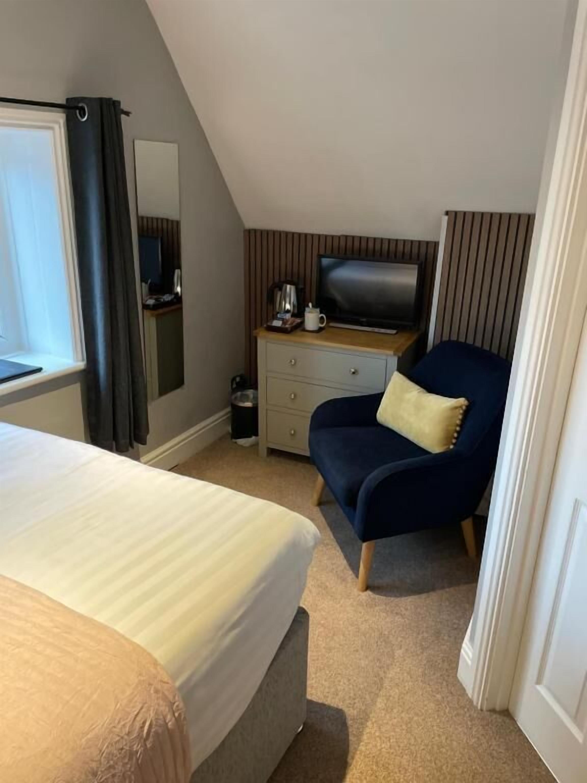 A hotel room with a bed, a desk with a television, a chair, and a window with curtains.