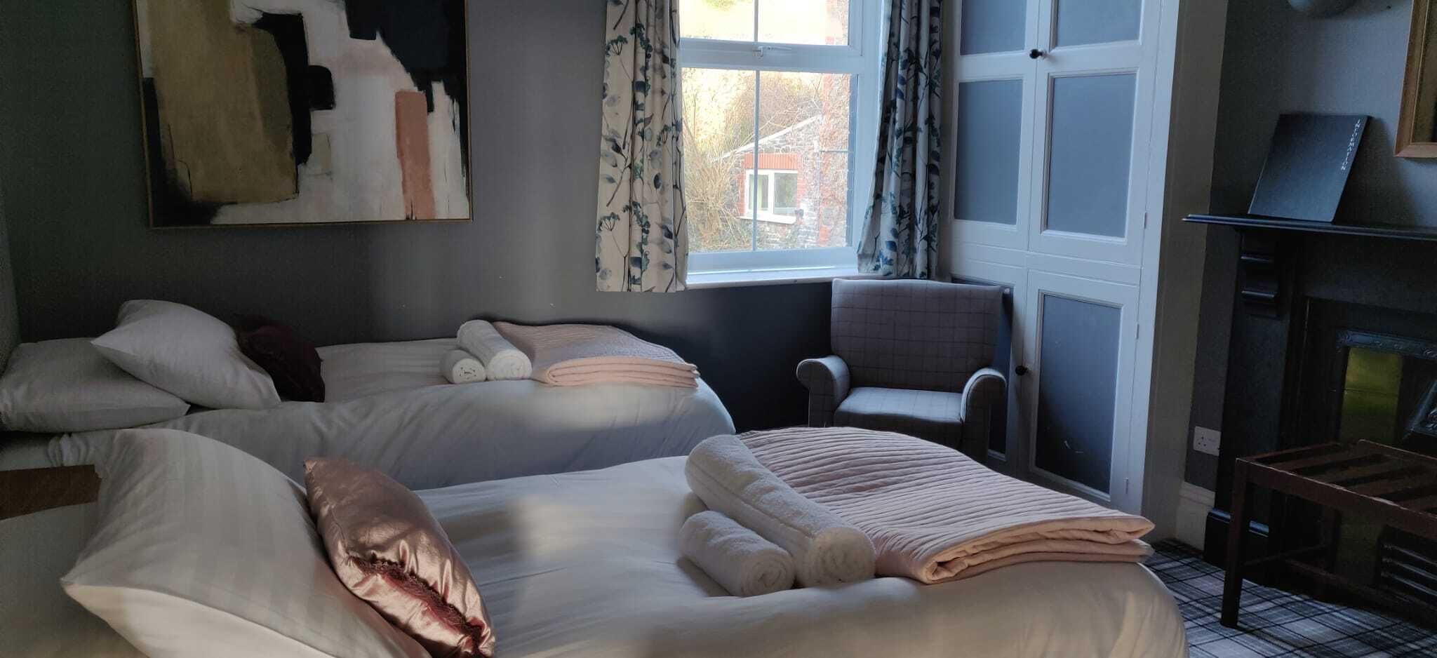 Une chambre d’hôtel avec deux lits, une chaise, une cheminée et une fenêtre avec des rideaux.