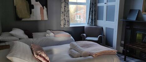 Une chambre d’hôtel avec deux lits, une chaise, une cheminée et une fenêtre avec des rideaux.